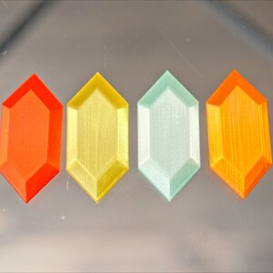 May include: Six different colored plastic gems in the shape of a hexagon. The gems are arranged in a row from left to right: blue, orange, yellow, light green, orange, and pink.