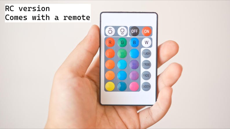 May include: A white remote control with colored buttons is held in a hand. The remote has buttons labeled "OFF" and "ON", and also includes color options and special effects like "FLASH" and "FADE". The text "RC version Comes with a remote" is visible.