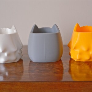 May include: Three 3D printed planters in white, gray, and orange. Each planter has a unique, textured design.