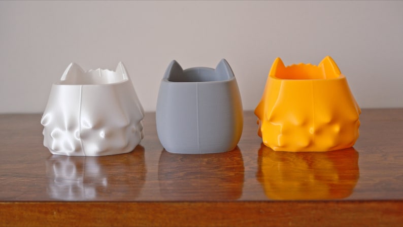 May include: Three 3D printed planters in white, gray, and orange. Each planter has a unique, textured design.