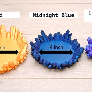 May include: Three crystal dish trays in different sizes and colours. The largest tray is 5 inches wide and gold, the middle tray is 4 inches wide and midnight blue, and the smallest tray is 3 inches wide and iridescent purple.