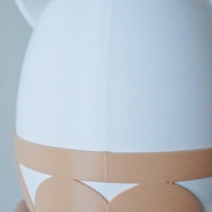 May include: White ceramic planter with a light brown rim and a scalloped design. The planter has two small ears on the top.