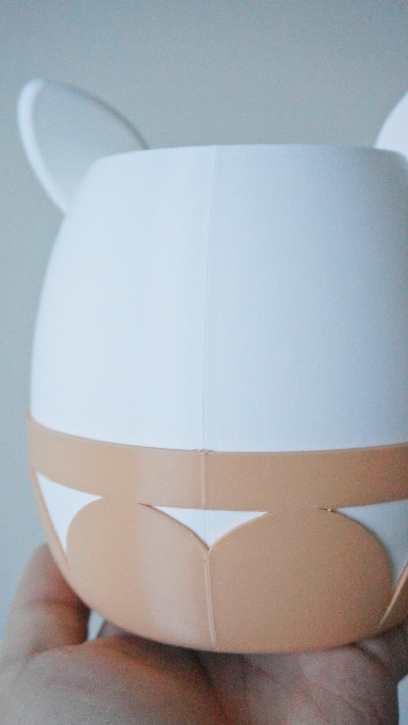 May include: White ceramic planter with a light brown rim and a scalloped design. The planter has two small ears on the top.