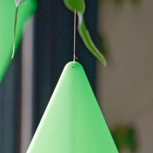 May include: A green, cone-shaped insect trap hangs from a string. The trap is made of a thin, flexible material and has a small hole at the top.