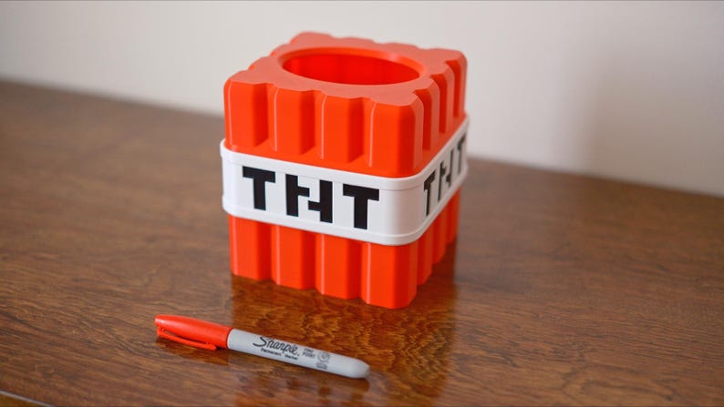 K&ouml;nnte beinhalten: Ein roter und wei&szlig;er Plastikbeh&auml;lter in Form eines Minecraft TNT-Blocks. Der Beh&auml;lter hat ein wei&szlig;es Band um sich herum mit dem Wort "THT" in schwarzen Buchstaben.