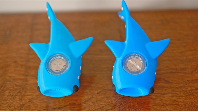 May include: Two blue whale shark shaped toys with a white spot on each side. The toys have a clear plastic circle in the center with a silver screw in the middle.