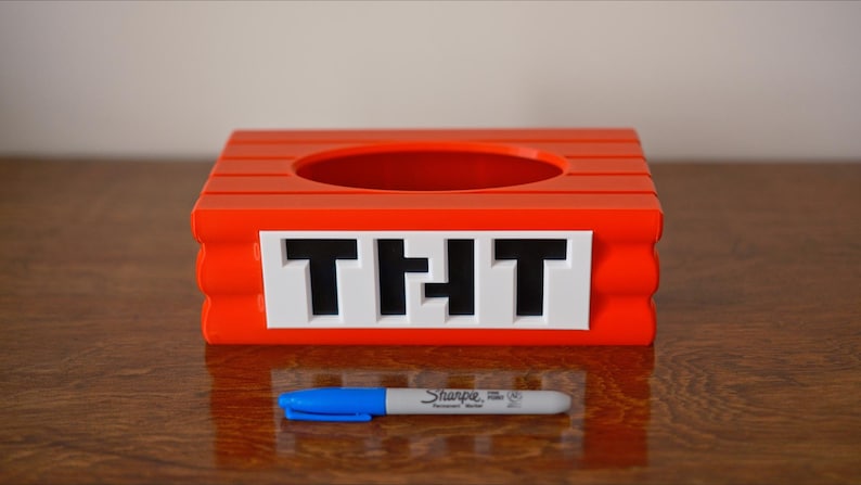 May include: A red plastic container with a round opening and the word "THT" printed on the front. The container is sitting on a wooden surface.