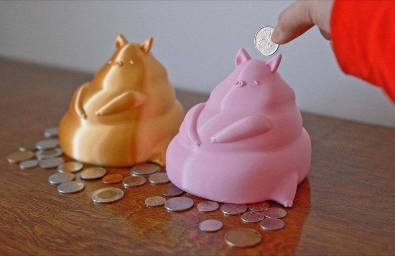 Gold and light pink piggy bank surrounded by coins with a hand dropping a coin into the piggy bank