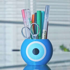 May include: Blue and white evil eye desk organizer with a variety of pens and scissors inside.