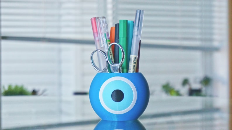 May include: Blue and white evil eye desk organizer with a variety of pens and scissors inside.