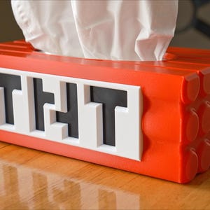 May include: A red tissue box holder shaped like a brick with the word "THAT" spelled out in black letters on a white background.