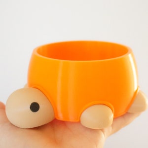 May include: Orange and beige ceramic turtle planter with a round opening. The planter is small and has a cute design.