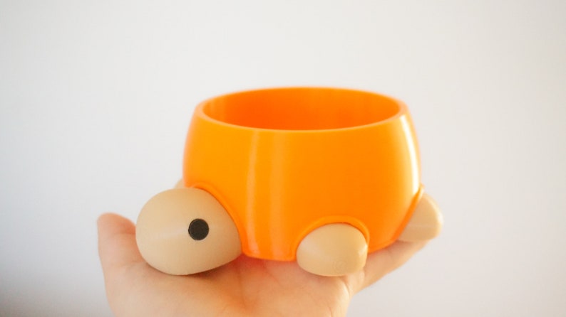 May include: Orange and beige ceramic turtle planter with a round opening. The planter is small and has a cute design.