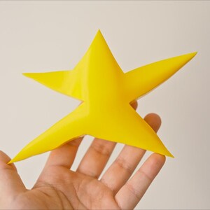 May include: A yellow 3D printed star with five points, held in a hand.