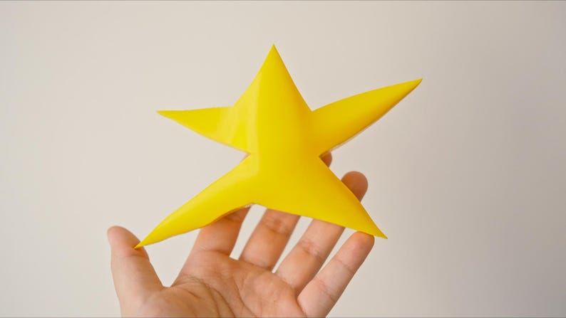 May include: A yellow 3D printed star with five points, held in a hand.