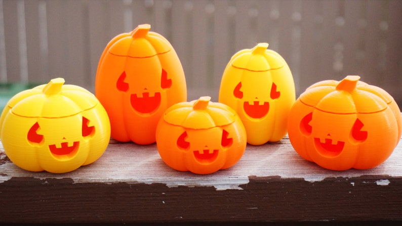 May include: Four orange and yellow plastic jack-o'-lantern candy holders with carved faces. The holders are different sizes and are arranged on a wooden surface.