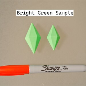 May include: Two bright green diamond-shaped plastic objects, one larger than the other, on a light gray surface. A red and white Sharpie fine point permanent marker is also on the surface. The text "Bright Green Sample" is at the top of the image.
