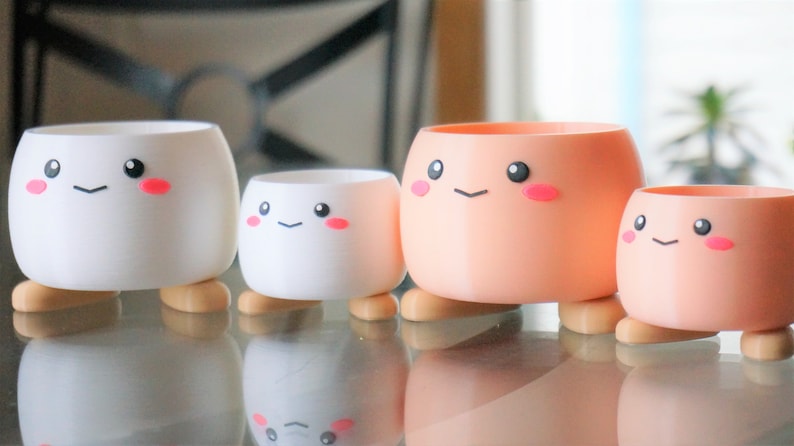 May include: Four small, colorful planters with cute cartoon faces and legs. The planters are made of plastic and are perfect for small plants or succulents.