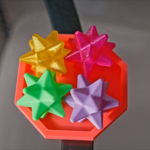 May include: Four colorful star-shaped objects in a red octagonal tray. The stars are yellow, pink, green, and purple.