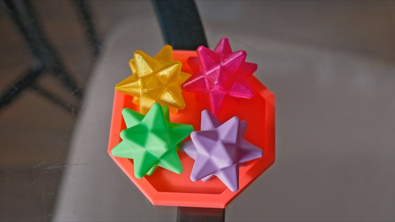 May include: Four colorful star-shaped objects in a red octagonal tray. The stars are yellow, pink, green, and purple.