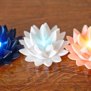 May include: Three lotus-shaped candles with LED lights. The candles are in shades of blue, white, and peach.