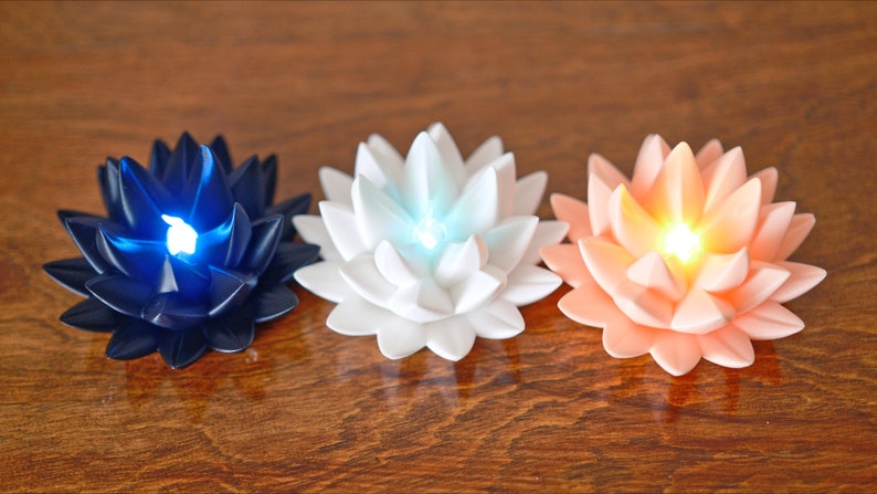 May include: Three lotus-shaped candles with LED lights. The candles are in shades of blue, white, and peach.
