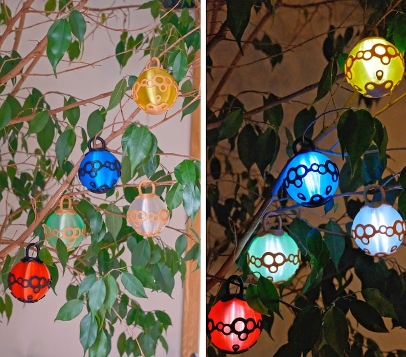 May include: A collection of colorful, spherical decorative lights hanging from the branches of a leafy green plant. The lights are in various colors, including yellow, blue, green, white, and red, with a black decorative pattern. The lights are illuminated in the second image.