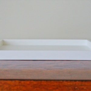 May include: A white rectangular tray with a raised edge. The tray is sitting on a wooden surface.