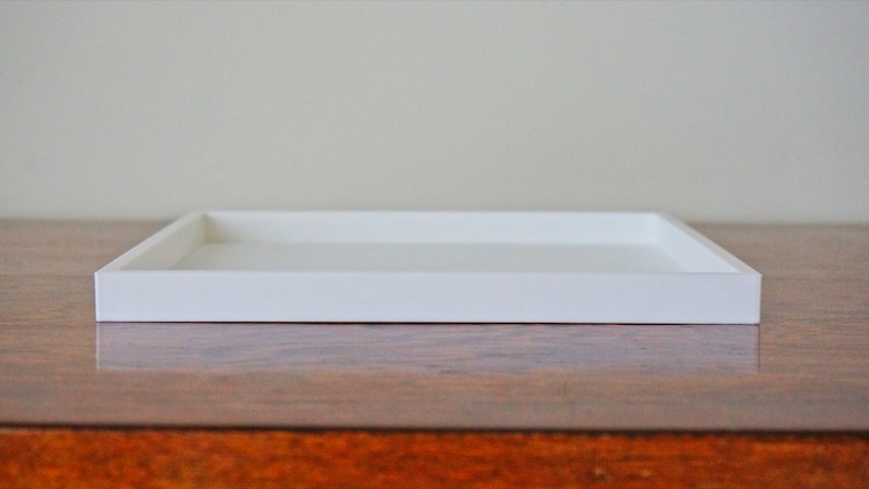May include: A white rectangular tray with a raised edge. The tray is sitting on a wooden surface.