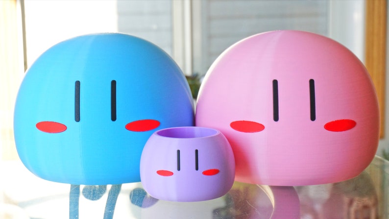 May include: Three dango figurines, one blue, one pink, and one purple. Each figurine has a simple face with two black eyes and two red cheeks.