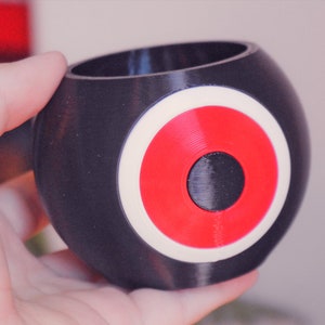 May include: A black and white planter with a red circle in the center. The planter is shaped like a sphere.