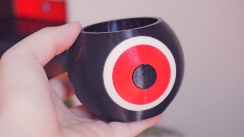 May include: A black and white planter with a red circle in the center. The planter is shaped like a sphere.