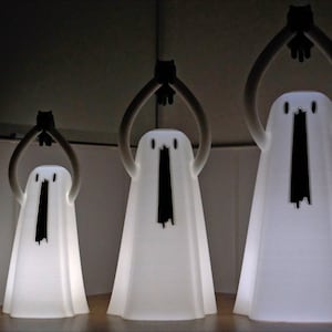 Peut inclure: Trois lampes blanches en forme de fant&ocirc;me avec des yeux et une bouche noirs, pos&eacute;es sur une surface en bois. Les fant&ocirc;mes ont les bras lev&eacute;s au-dessus de leur t&ecirc;te.