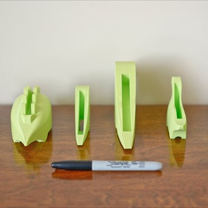 May include: A set of six lime green 3D printed phone stands of varying sizes. The stands are arranged in a row on a wooden surface.