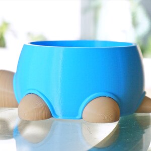 May include: A blue ceramic pet bowl shaped like a turtle with wooden legs. The bowl is empty and ready for food or water.