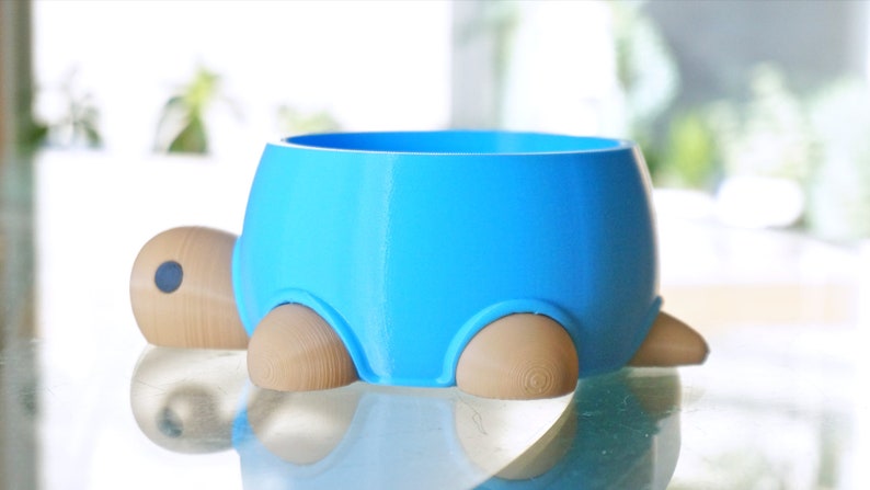 May include: A blue ceramic pet bowl shaped like a turtle with wooden legs. The bowl is empty and ready for food or water.