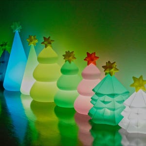 Può includere: Una fila di decorazioni per alberi di Natale illuminate in vari colori, tra cui verde, blu e rosa. Ogni albero ha una stella in cima. Gli alberi sono disposti in fila, creando un'esposizione festosa e colorata.