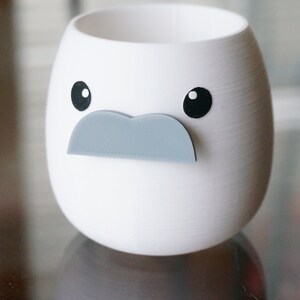 May include: White ceramic planter shaped like a face with black eyes and a gray mustache.