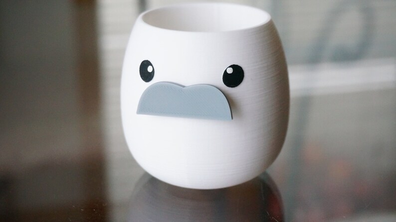 May include: White ceramic planter shaped like a face with black eyes and a gray mustache.