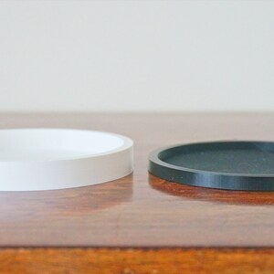 Puede incluir: Dos posavasos redondos, uno blanco y uno negro, sobre una superficie de madera.