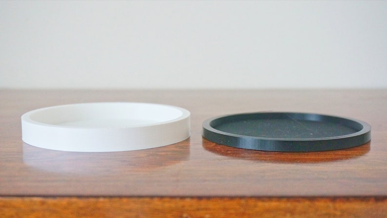 Puede incluir: Dos posavasos redondos, uno blanco y uno negro, sobre una superficie de madera.