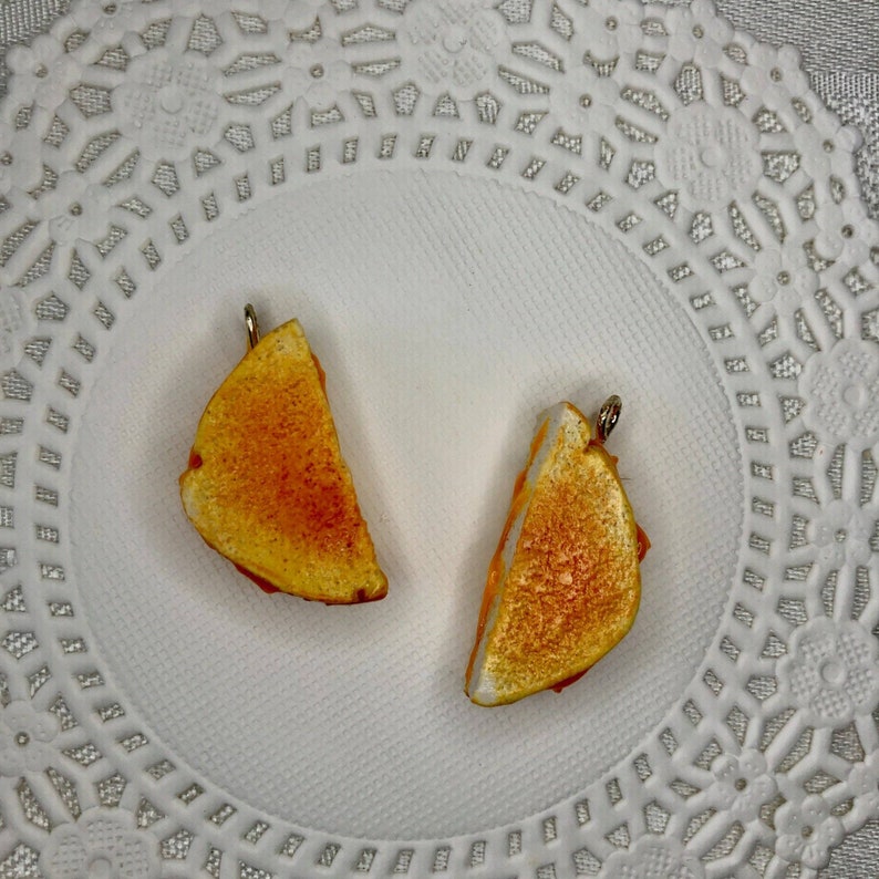 May include: Two miniature grilled cheese sandwiches with a golden brown crust and a hint of orange inside. The sandwiches are on a white doily.
