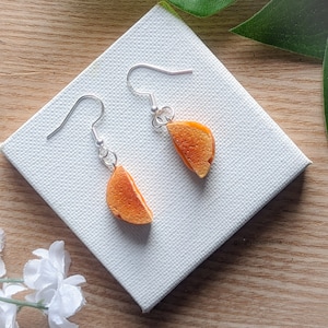 May include: A pair of orange and brown dangle earrings shaped like a half-circle sandwich. The earrings are made of polymer clay and have silver hooks.