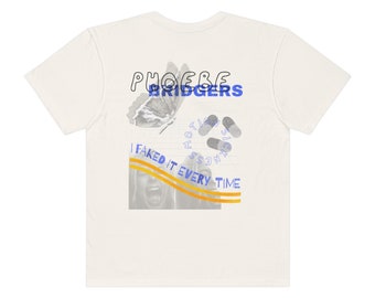 Op de afbeelding: Wit T-shirt met een grafisch ontwerp met de tekst "Phoebe Bridgers" in blauw, een vlinder, pillen en de tekst "I faked it every time" in geel.