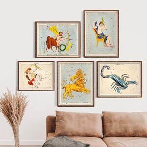 May include: Five framed vintage constellation prints. The prints feature colourful illustrations of zodiac signs like Sagittarius, Capricorn, Gemini, Leo, and Scorpio. The prints are displayed on a white wall above a brown sofa with a green blanket.