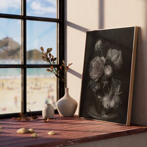 May include: A framed black and white print of a bouquet of peonies in a vase, sitting on a wooden windowsill with a view of a beach and a distant town. There are two small white ceramic vases and seashells on the windowsill.