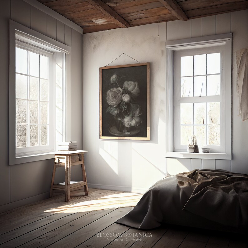 May include: A vintage still life painting of white flowers in a vase, hanging on a white wall in a room with two windows and a wooden floor. The painting is framed in a gold frame and has the text "BLOSSOM BOTANICA Vintage Art Collective" at the bottom.