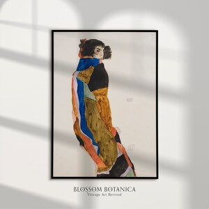 May include: A vintage art print of a woman in a colorful, geometric patterned dress. The woman is standing with her back to the viewer, looking over her shoulder. The print is in a black frame.