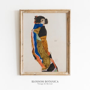 May include: A framed print of a painting depicting a woman in a colorful patterned dress and a blue scarf. The woman is standing with her back to the viewer and her head turned to the side. The painting is in a light wood frame.