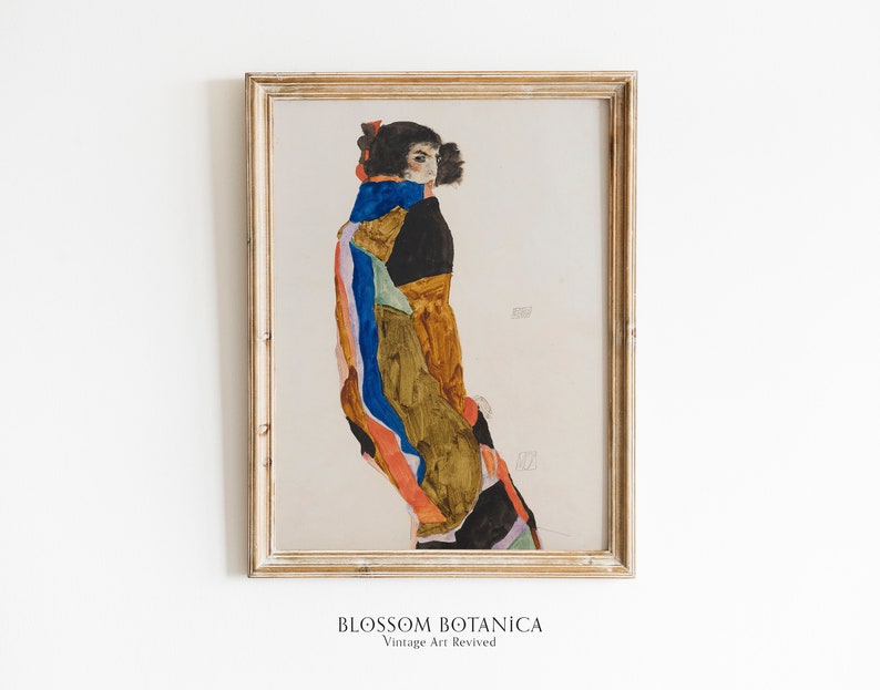 May include: A framed print of a painting depicting a woman in a colorful patterned dress and a blue scarf. The woman is standing with her back to the viewer and her head turned to the side. The painting is in a light wood frame.